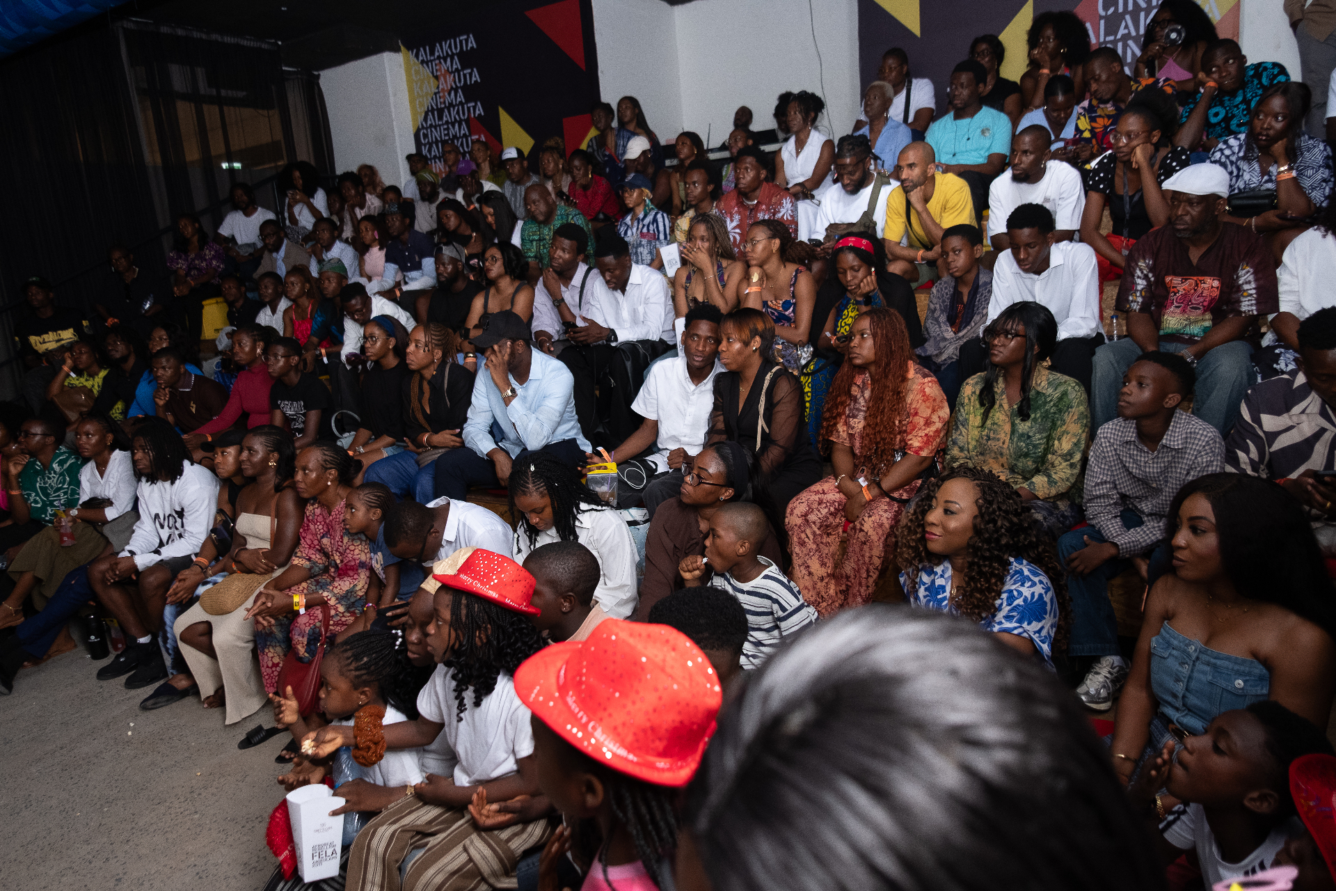Packed audience seated on the floor watching a film in front of the Kalakuta Cinema wall at Afrobeat Rebellion