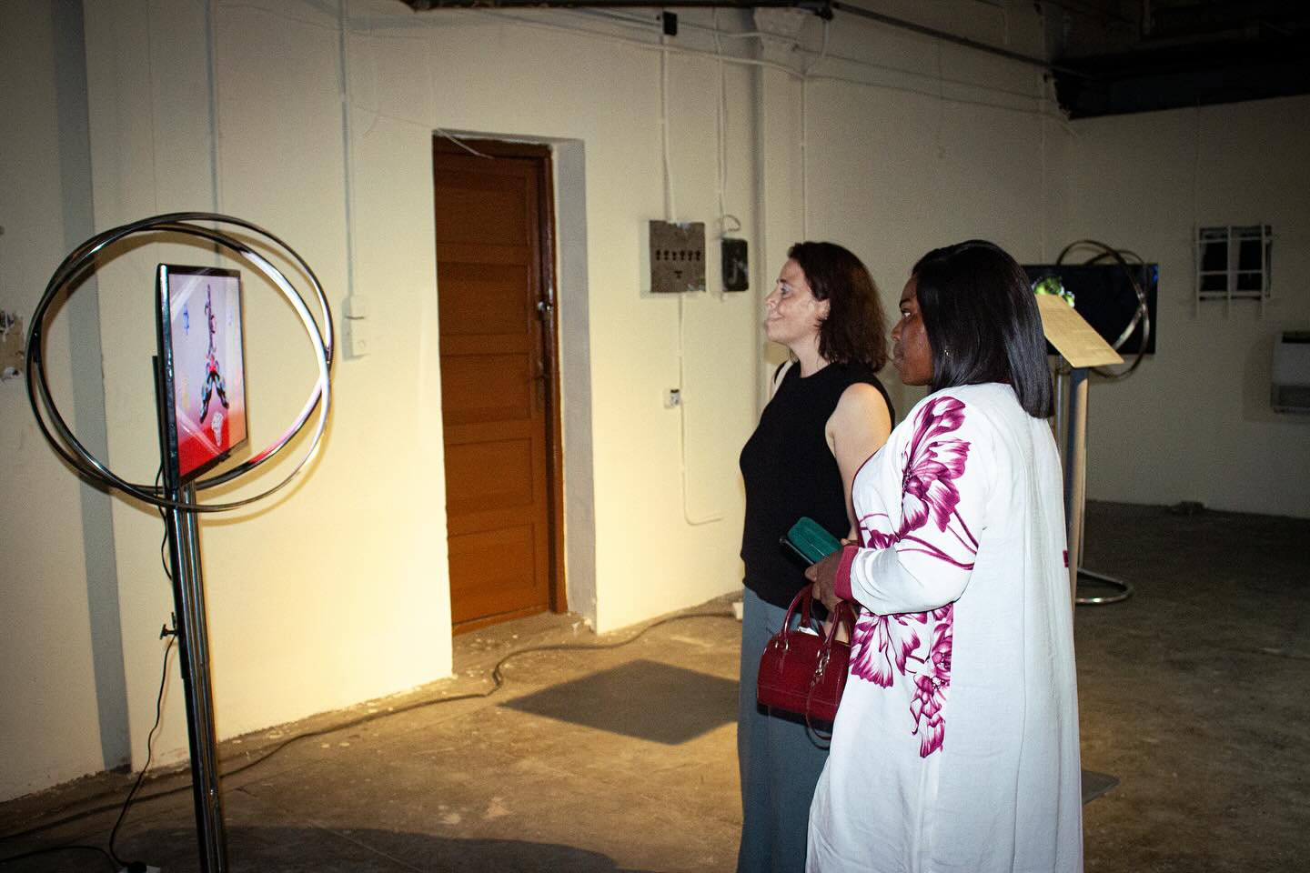 Two visitors watching a video artwork mounted inside a chrome ring frame at Kedu Lagos in the former Government Printing Press, Marina