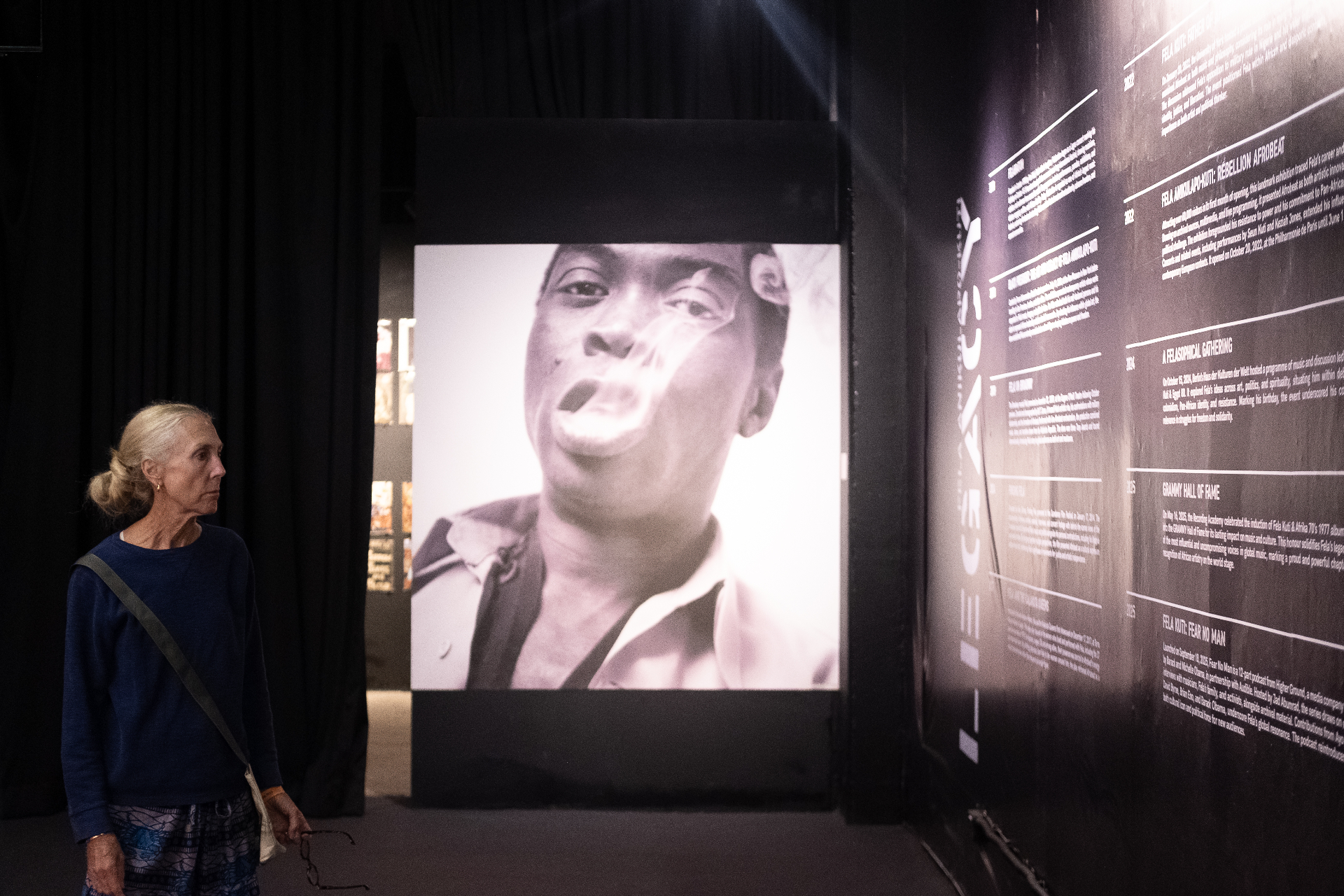 Visitor viewing a large projected portrait of Fela Kuti beside the Legacy timeline wall at Afrobeat Rebellion