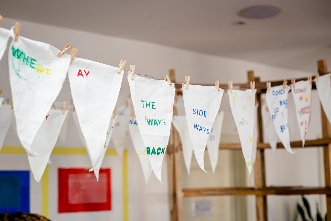 Pennant flags pegged to a line, each hand-printed with fragments of text in green, red and blue