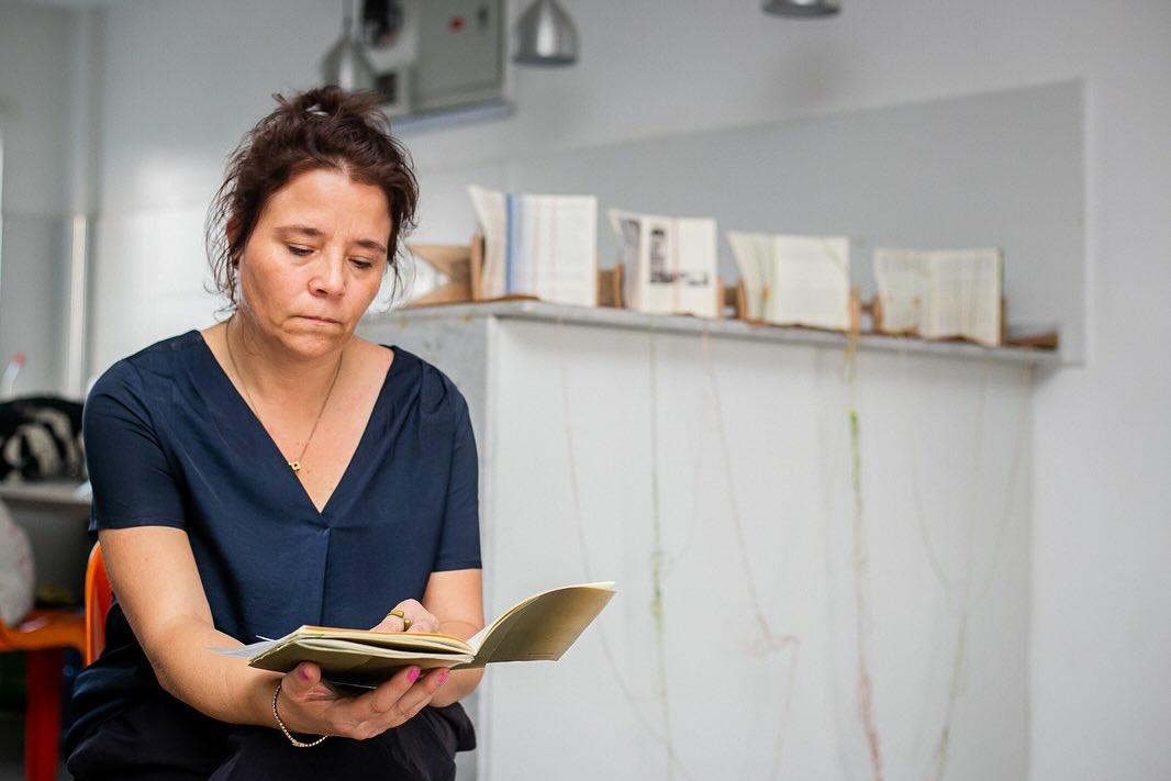 A visitor seated with a small book in hand, reading in front of a ledge of open publications from Write, If You Please