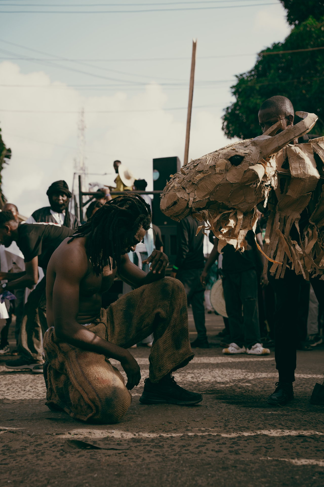 Performer kneeling on the street beside a cardboard animal puppet