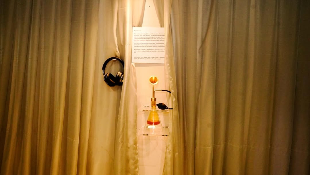 Scent-bottle station in the Sarauniya Ènè olfactory installation, headphones and an amber flask hanging beside curtain folds